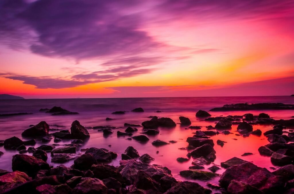 Beautiful seaside sunset with vibrant pink and orange colors against rocky shoreline.